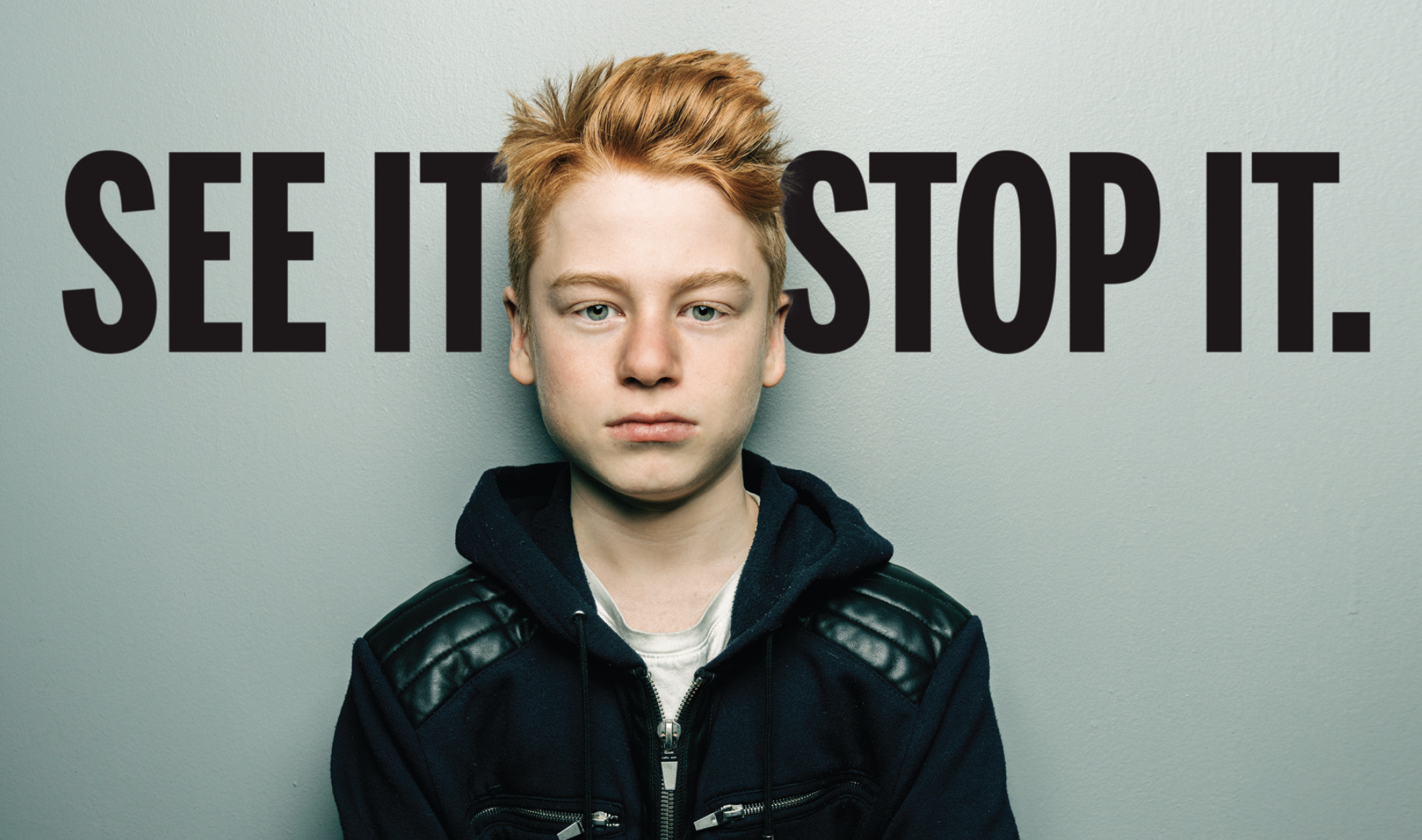 Red-haired boy standing in front of the words, "SEE IT, STOP IT."