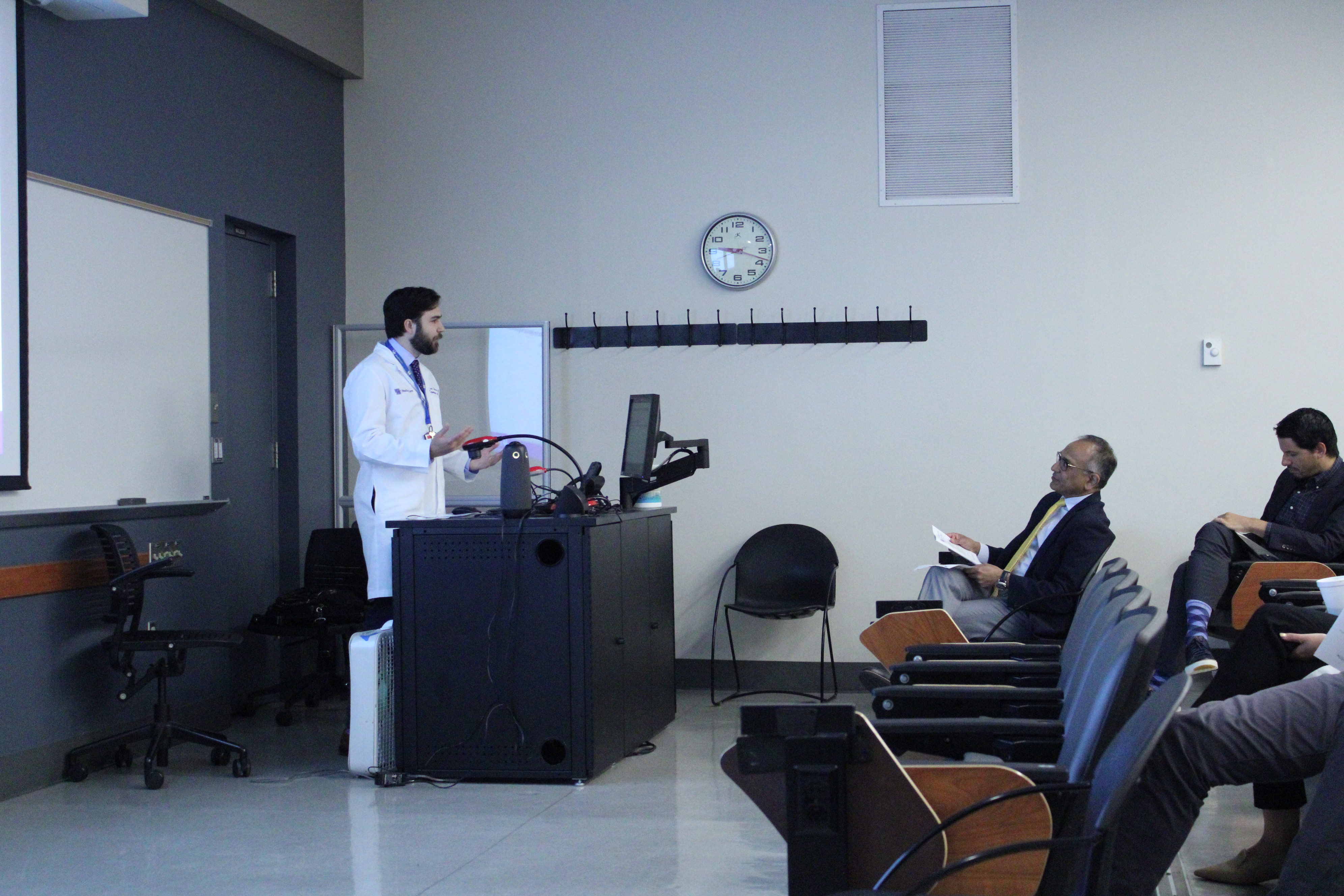 A UK student standing at a podium talking to Dr. Sundaram who is seated in an auditorium. 