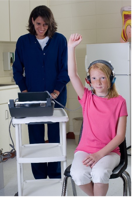 A girl in a pink shirt raises her hand to indicate to the woman behind her that she can hear the sound.