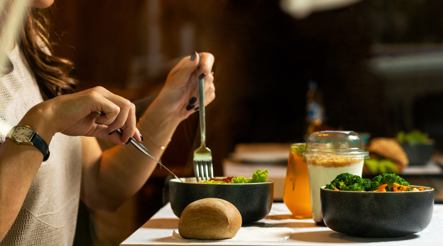 food on a table with a pair of hands using utensils to cut up food in a bowl