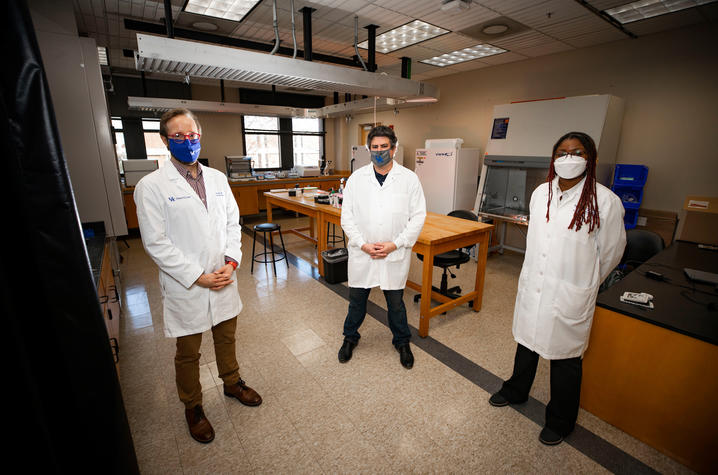 3 researchers standing apart with a laboratory in the background