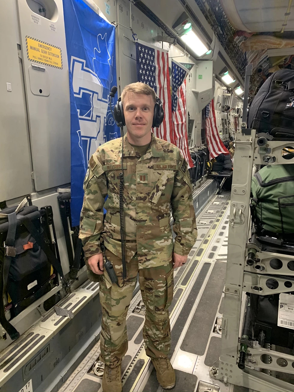 USAF Major, Dr. Chris Belcher on a C-17 deck in military uniform with USA and UK flags in background