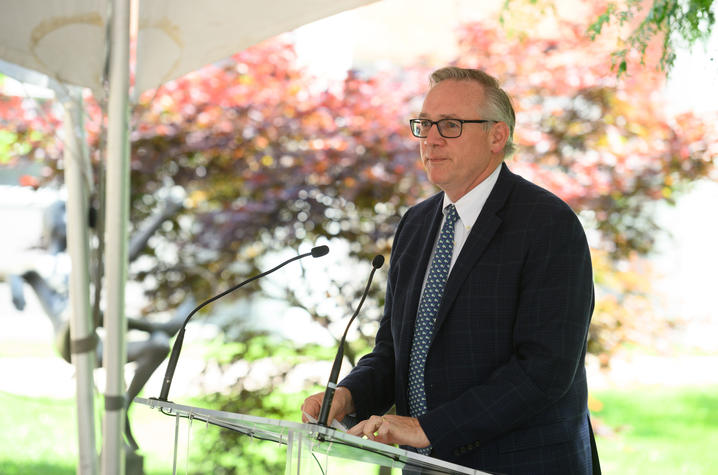 Dr. Stephen Strup stands at a glass podium looking serious. 