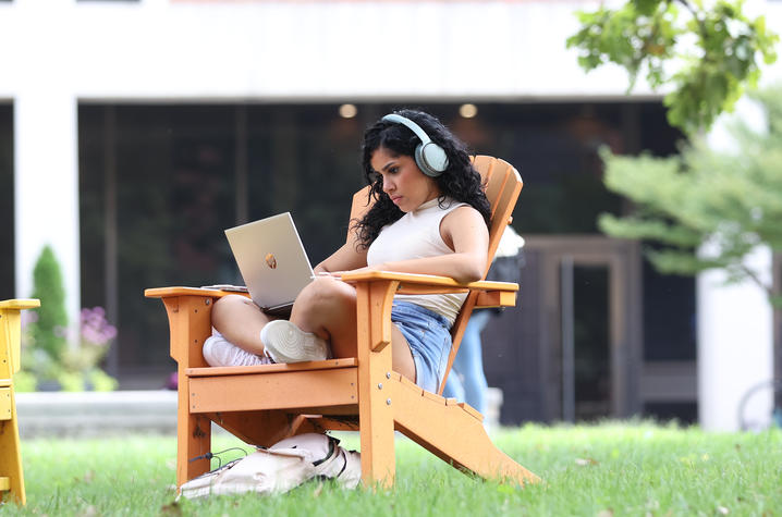 university student with headphones sitting in Adirondack chair and looking at computer screen