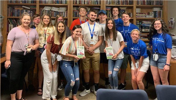 Group of high school and undergraduate students standing in front of shelves of books and smiling for a group photo