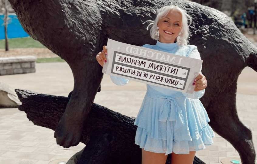 Madison Tackett standing in front of wildcat statute with sign states "I matched. Internal medicine at University of Kentucky."