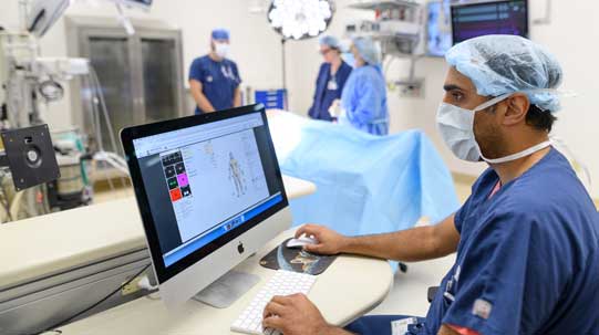 healthcare provider viewing a computer screen with simulation patient information; simulation operating room in background