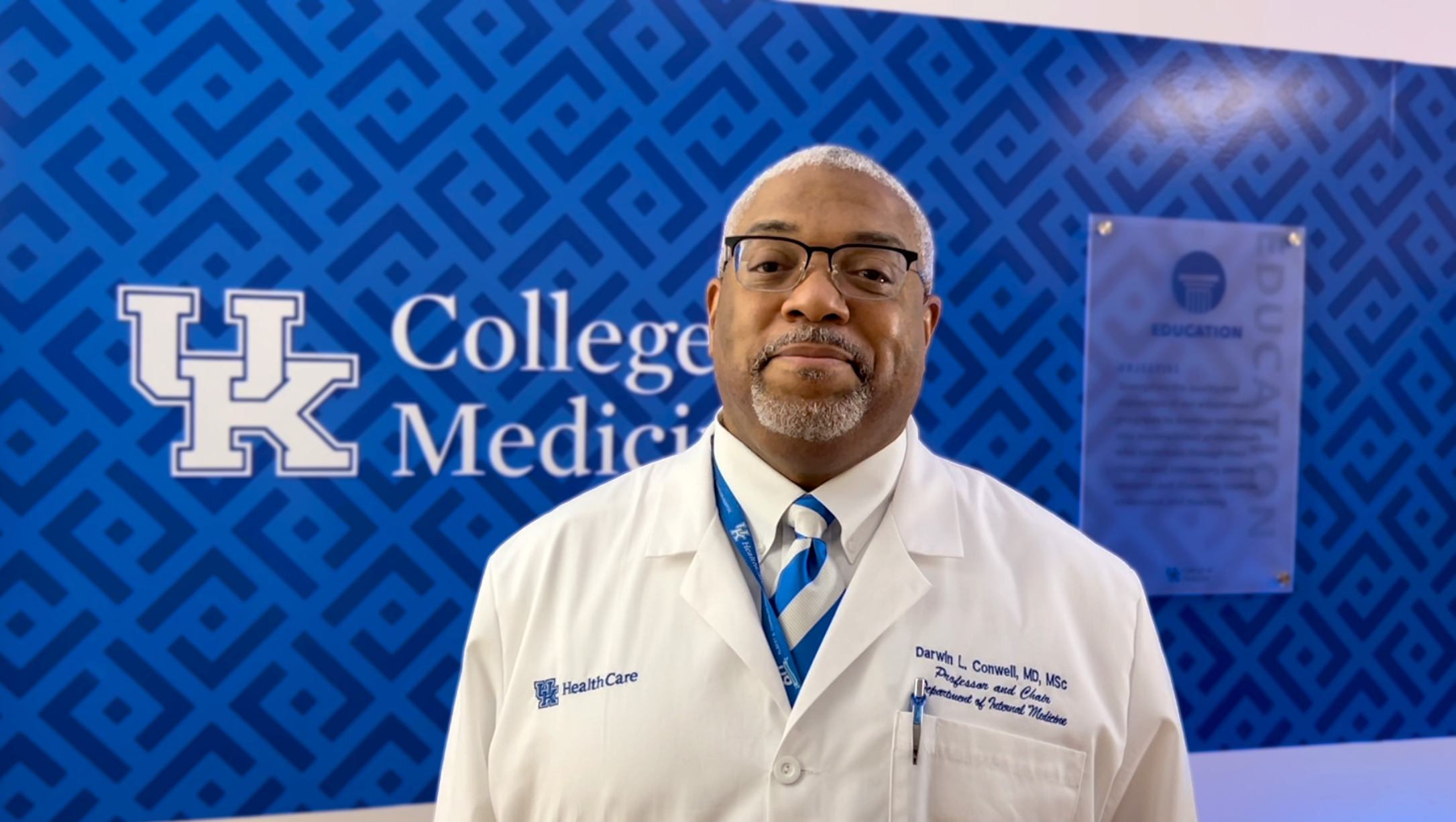 Darwin Conwell, MD in front of a blue UK College of Medicine wall