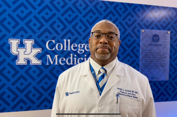 Darwin Conwell, MD, in a white coat, and in front of the blue, UK College of Medicine wall.