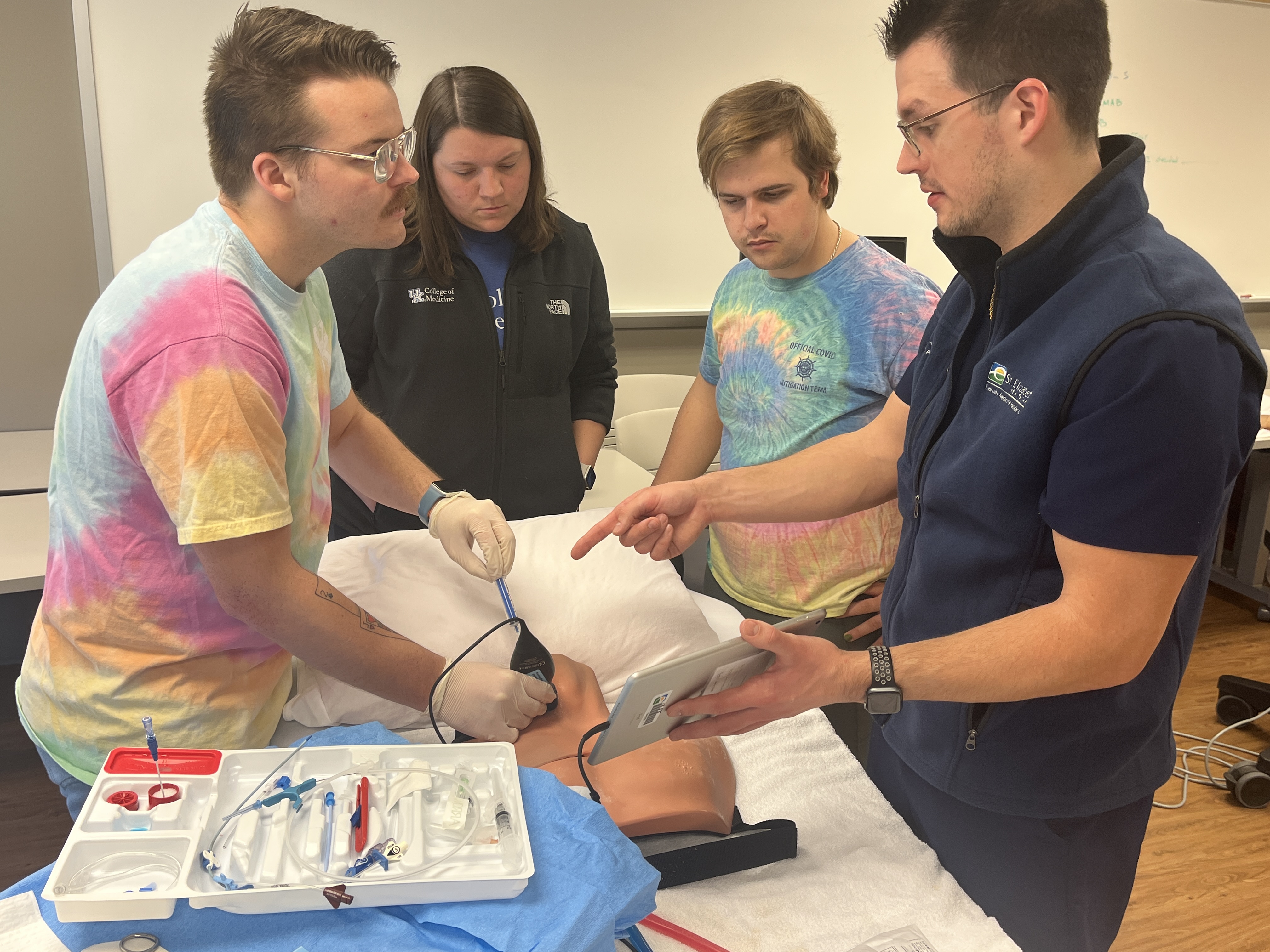 medical students receiving instruction from residents over a mannequin