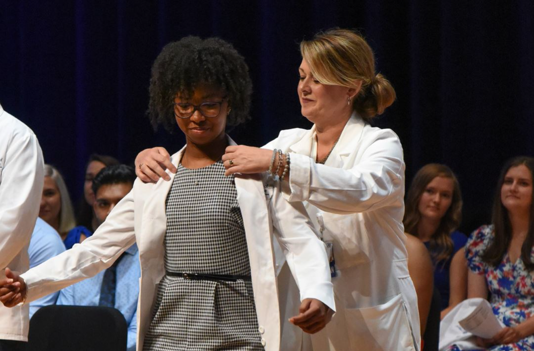 student receives her white coat during a ceremony