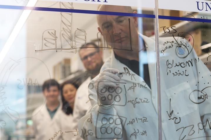 Terry Hinds, PhD, writing on a clear board with students in his lab.