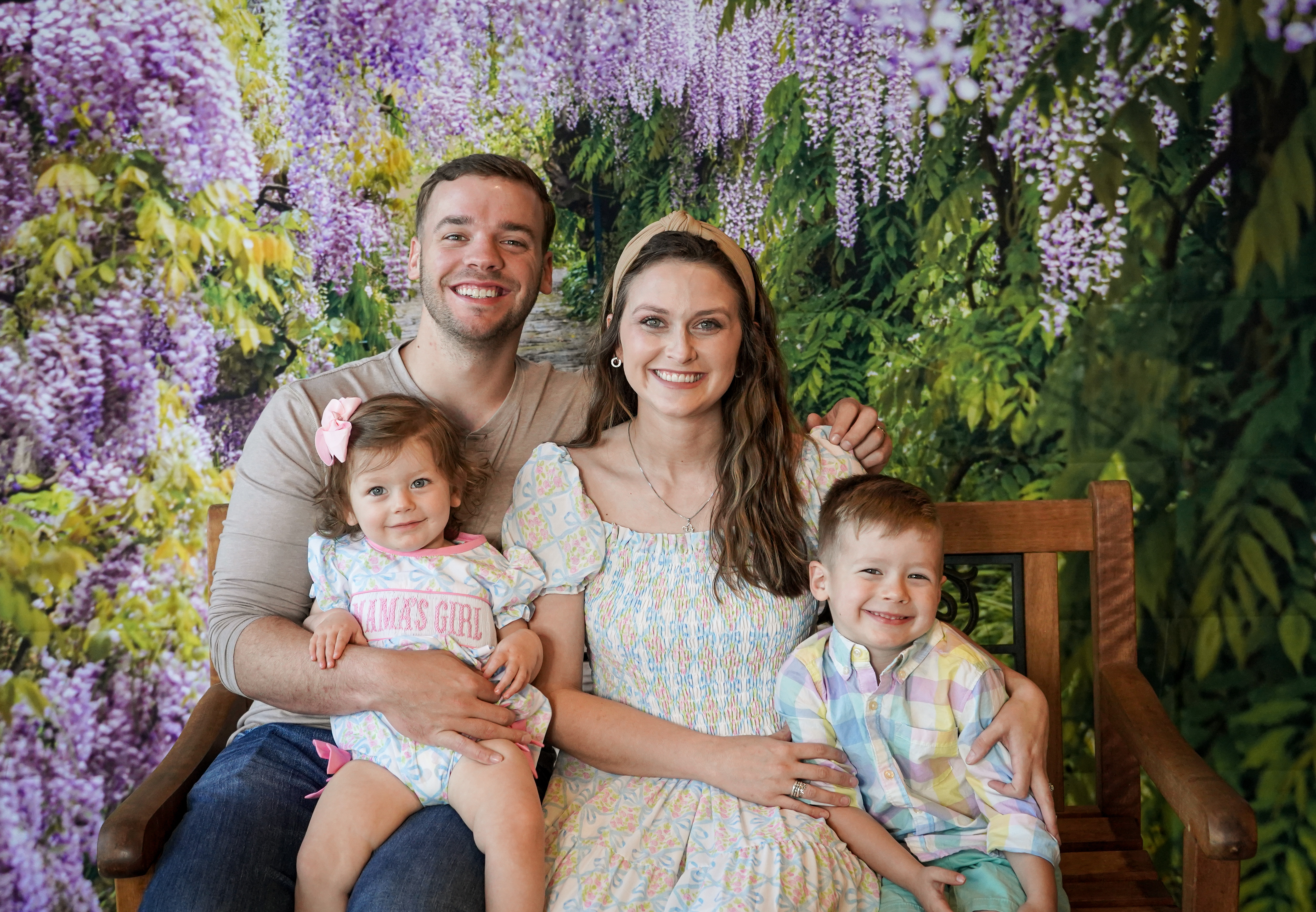 Ryan Harpole sitting with his wife and two kids in front of purple and green flowers. 