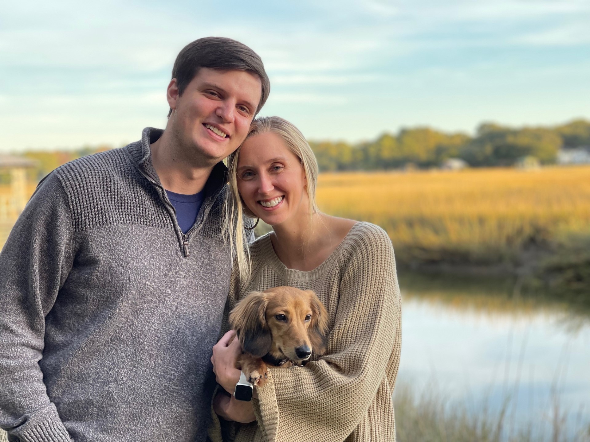 Cody Blanchard standing with his wife in front of a lake while they hold their dog. 