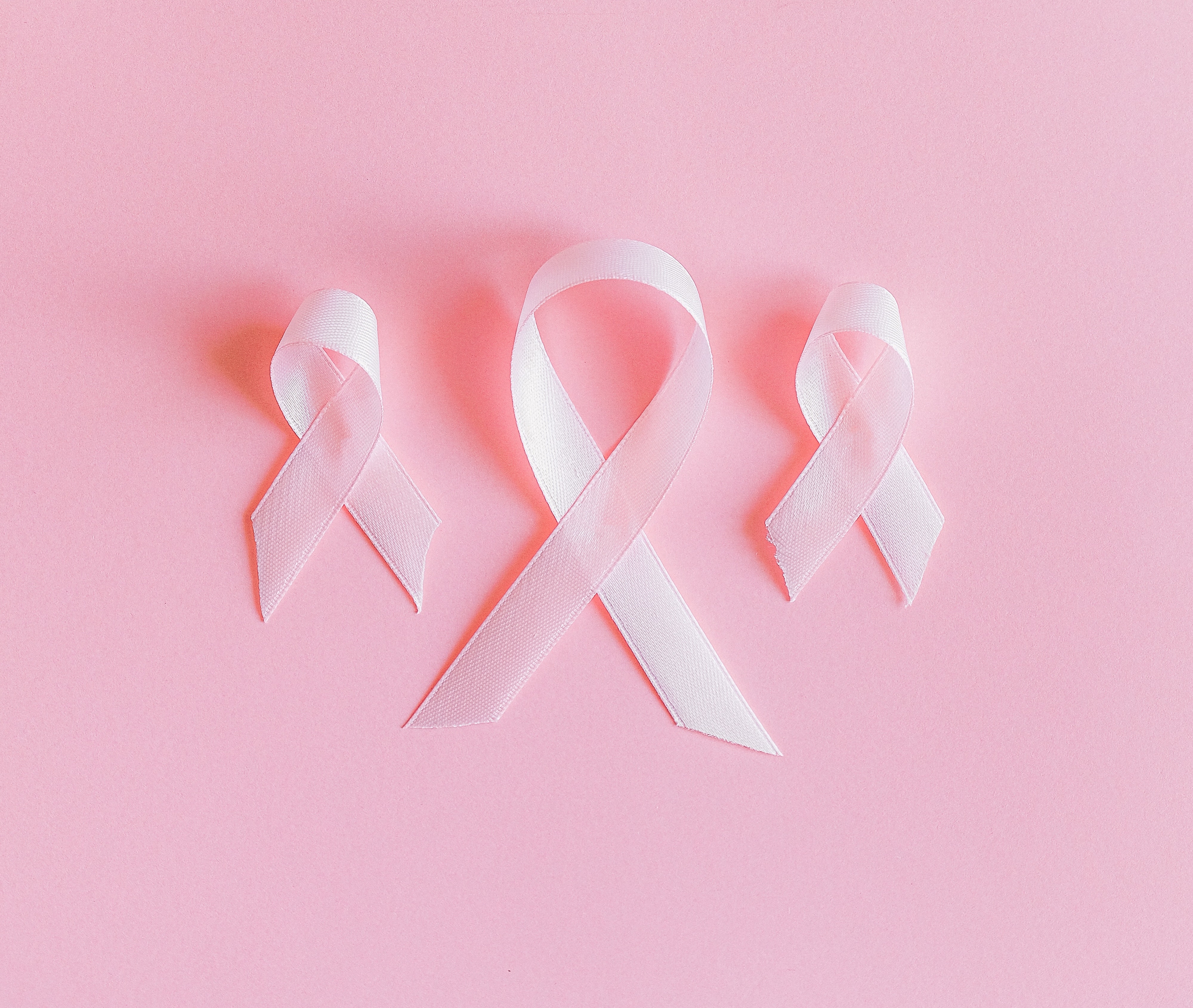 Three breast cancer awareness ribbons on a pink background.