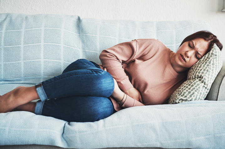 Woman hugging her stomach while curled up on a couch.