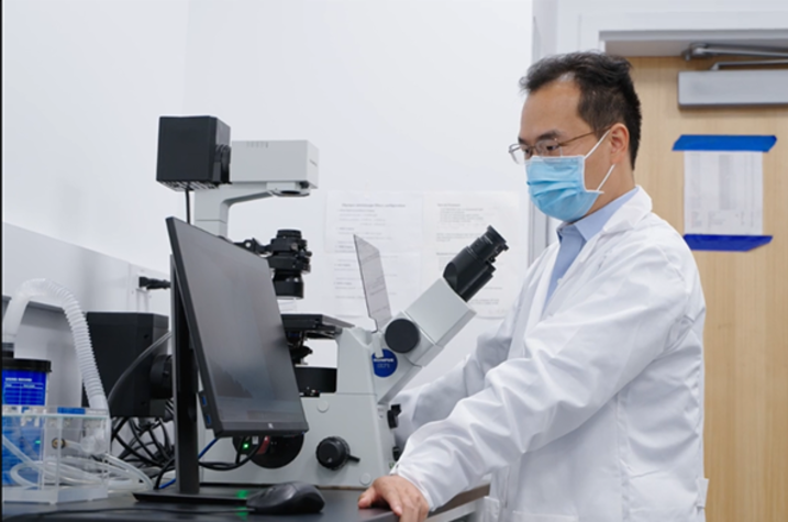 Caigang Zhu, PhD using a microscope.