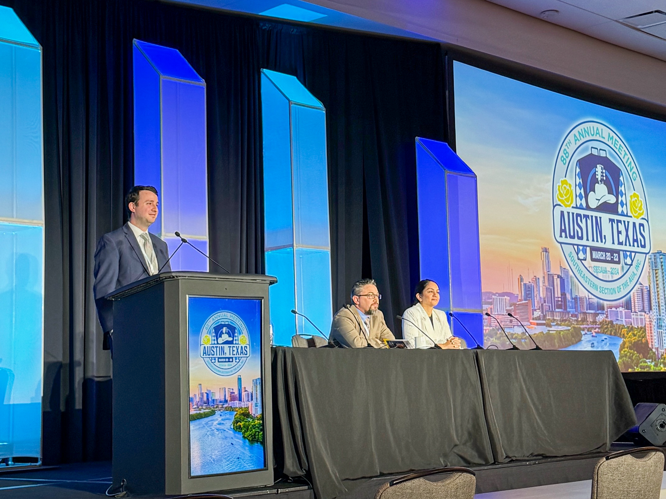 Dr. Seth Teplitsky presenting at a podium with a large screen behind him that SES AUA 2024