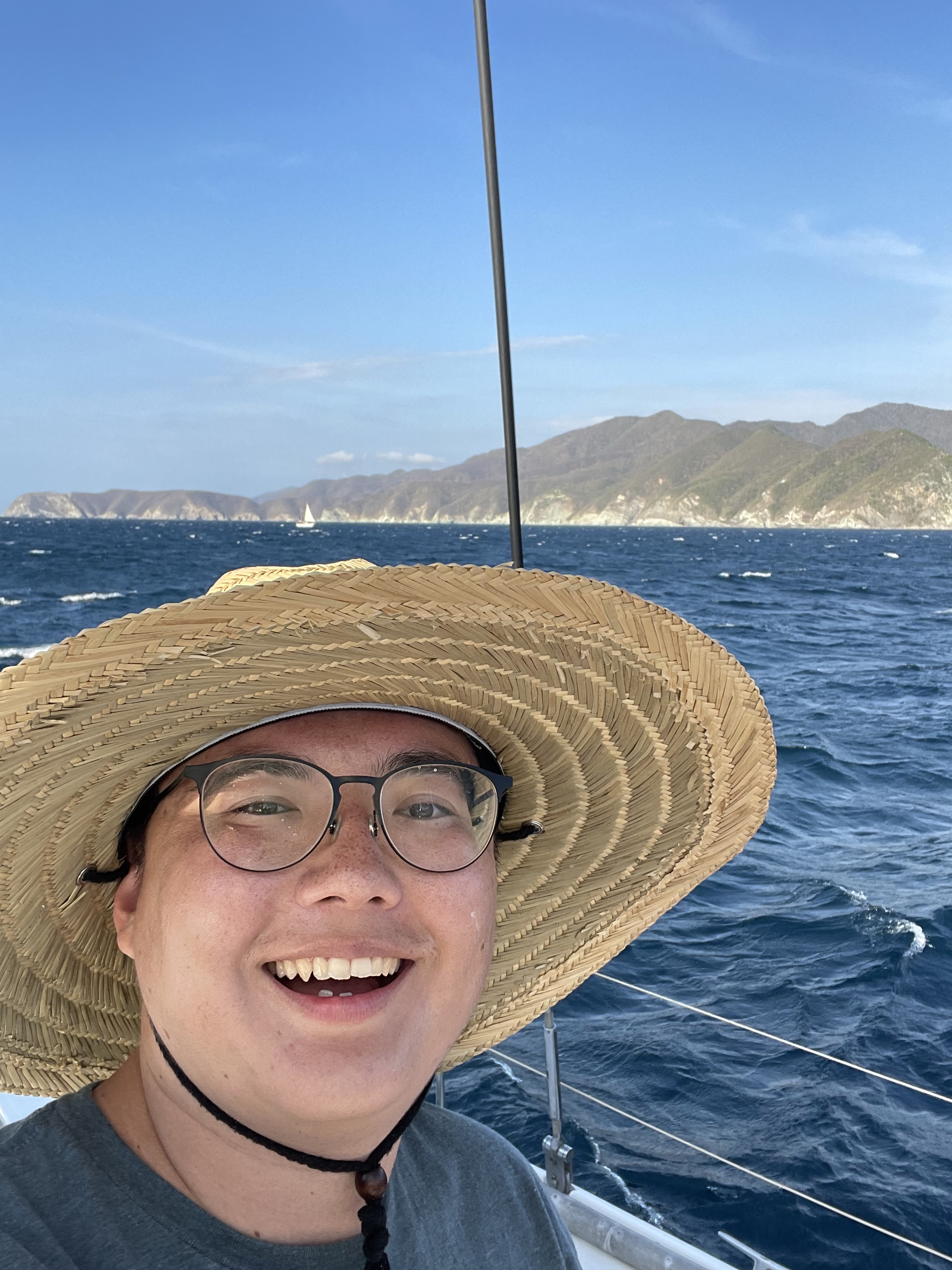 Resident Jaycob Avaylon wearing a sun hat smiling on a boat with the ocean in the background. 