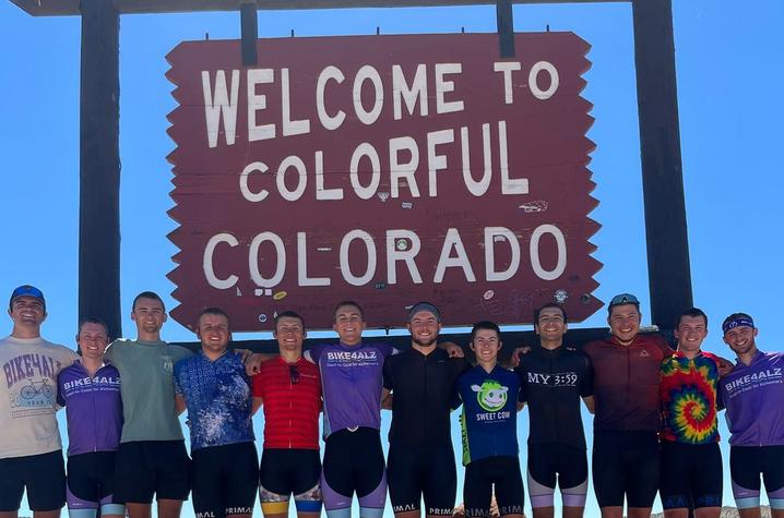 Bike4Alz team shoulder-to-shoulder in front of a sign that reads, "Welcome to Colorful Colorado"