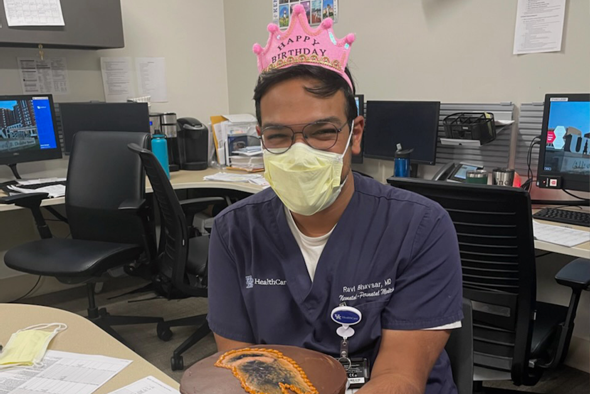Ravi Bhavsar on his birthday wearing a pink crown, and holding a cake with an image of his dog on it.