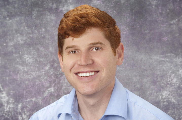 Professional headshot of Drew Micciche, a white man with red hair smiles, wearing a blue polo visible from the shoulders up.