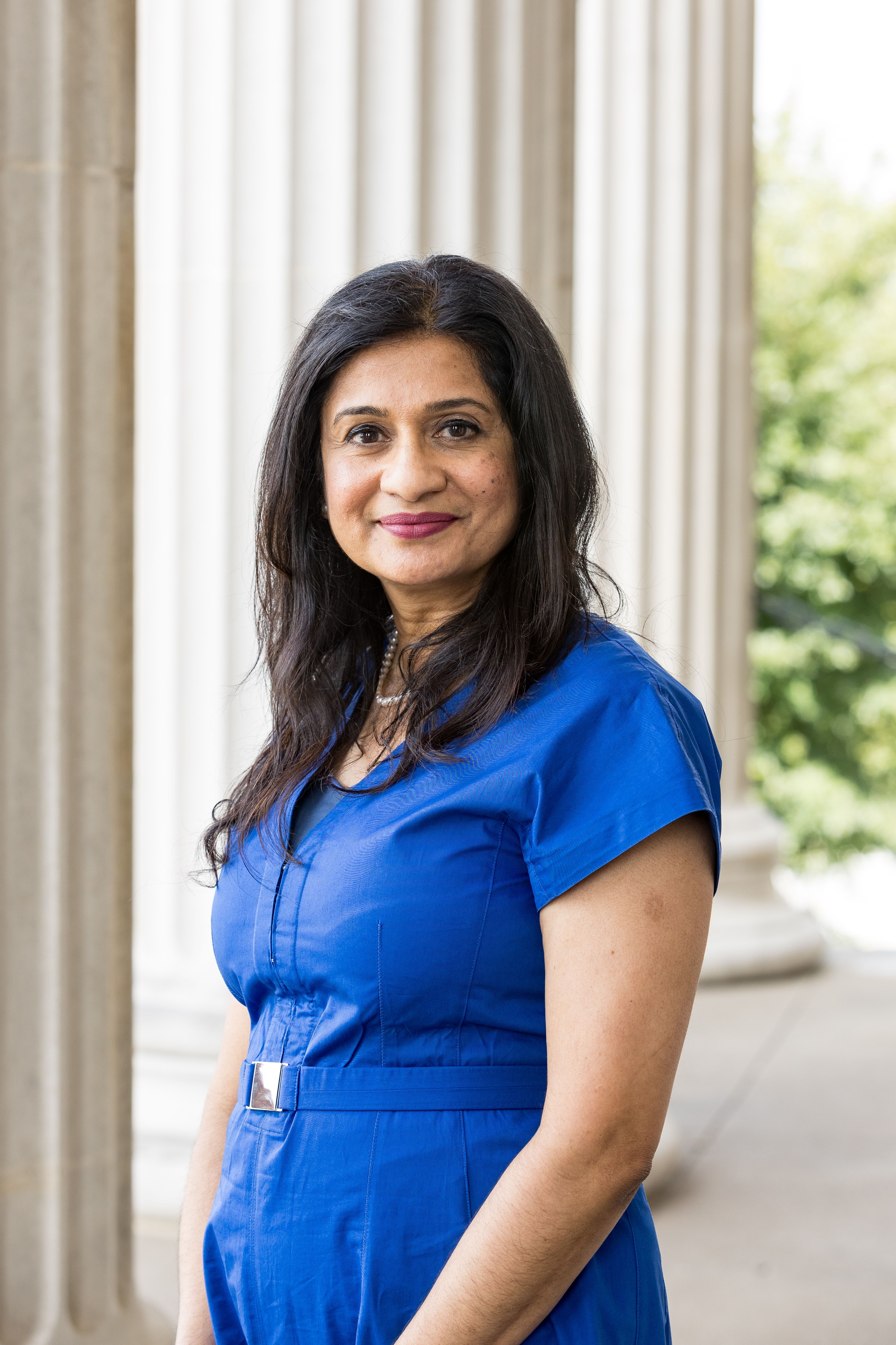 Caroline Paul, MD, stands in blue dress with shoulder-length dark hair