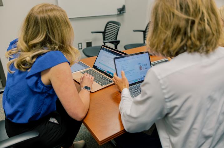 Two blond women working at laptops in a conference room.