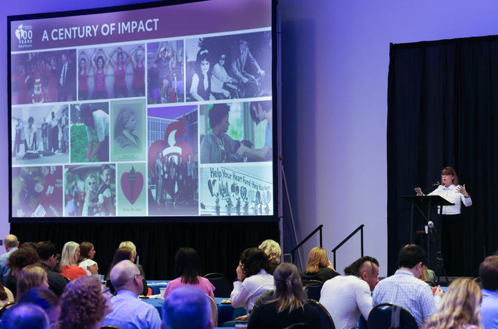 Nancy Brown presenting a talk on "A Century of Impact" to an auditorium of people.