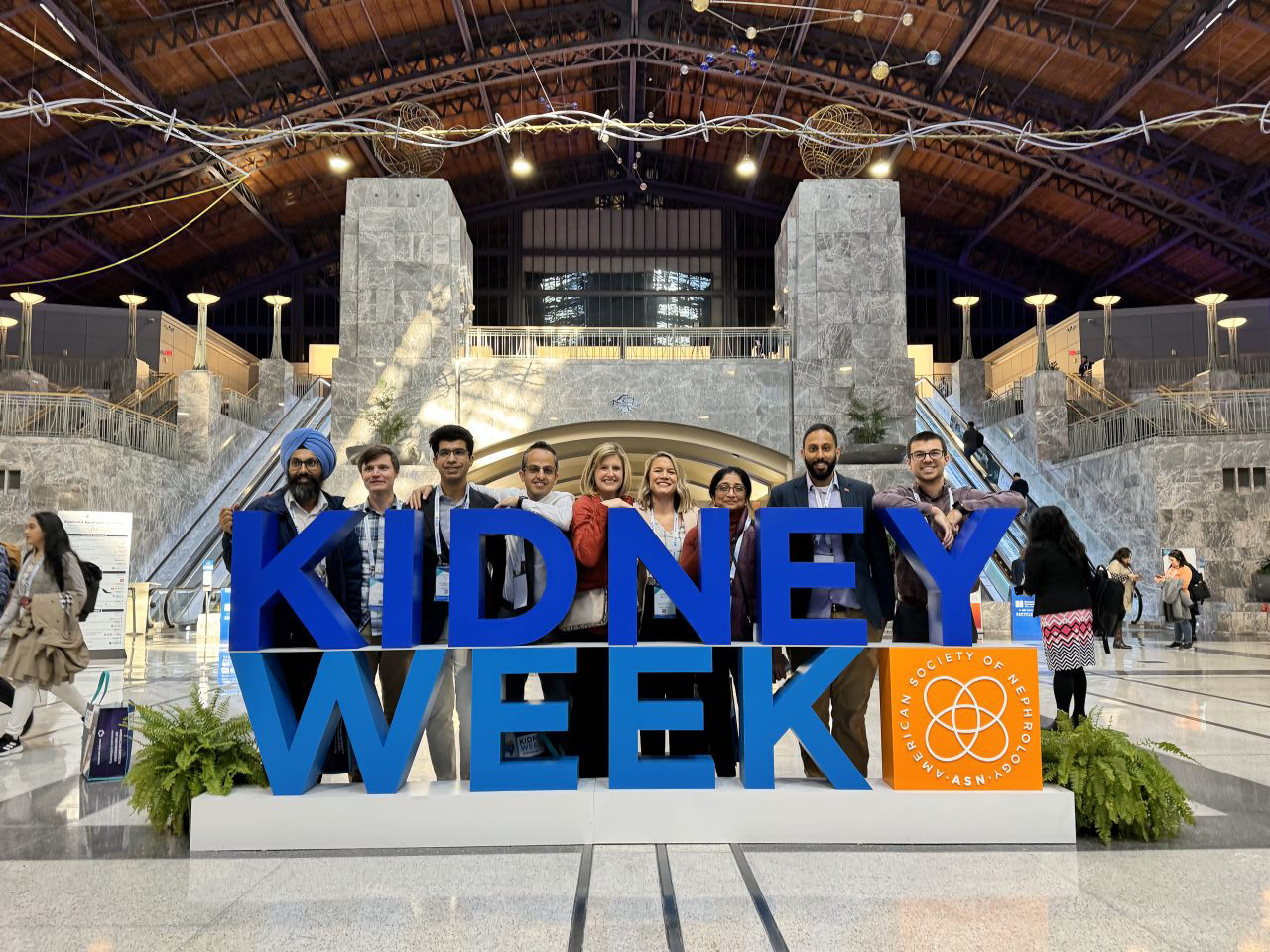 Nephrology Fellowship residents in a grand entry hall, behind a sign that reads, "Kidney Week - American Society of Nephrology (ASN)"