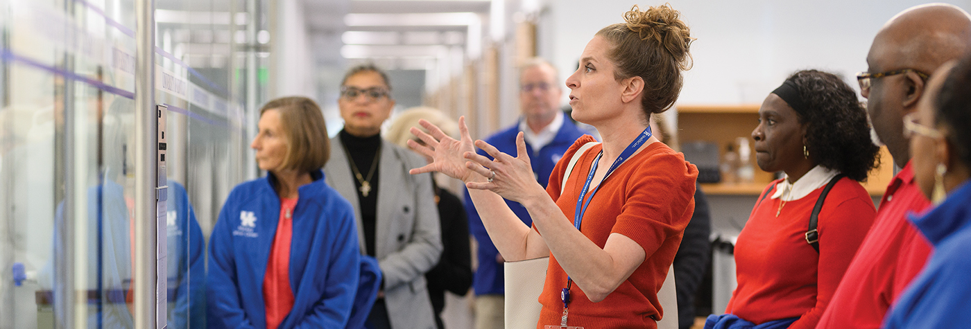 A woman gesturing while speaking to a large group of people.