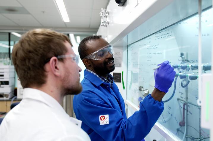 Two men working in a laboratory, while one writes on a white board