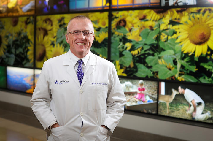 Scottie Day, MD, poses by the Kentucky Wall outside KCH, with both hands in the front pockets of his white coat