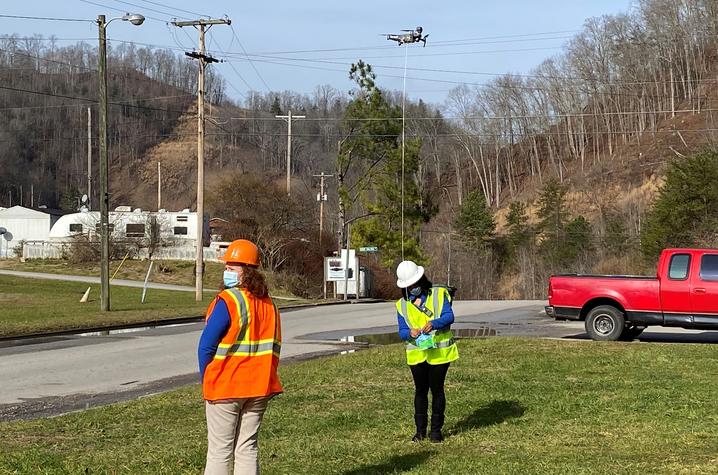 Chyna Smith, left, and Carole Frazier standing outdoors, wearing reflective safety vests as they retrieve a package delivery from a drone.