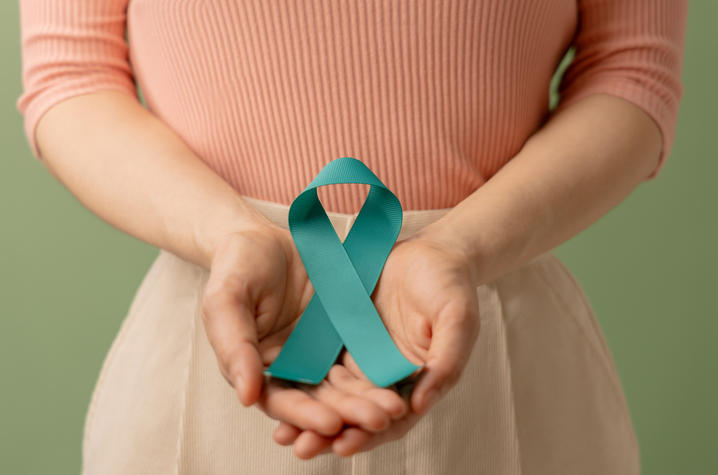 A woman cradling a teal cancer ribbon in both hands at waist height.