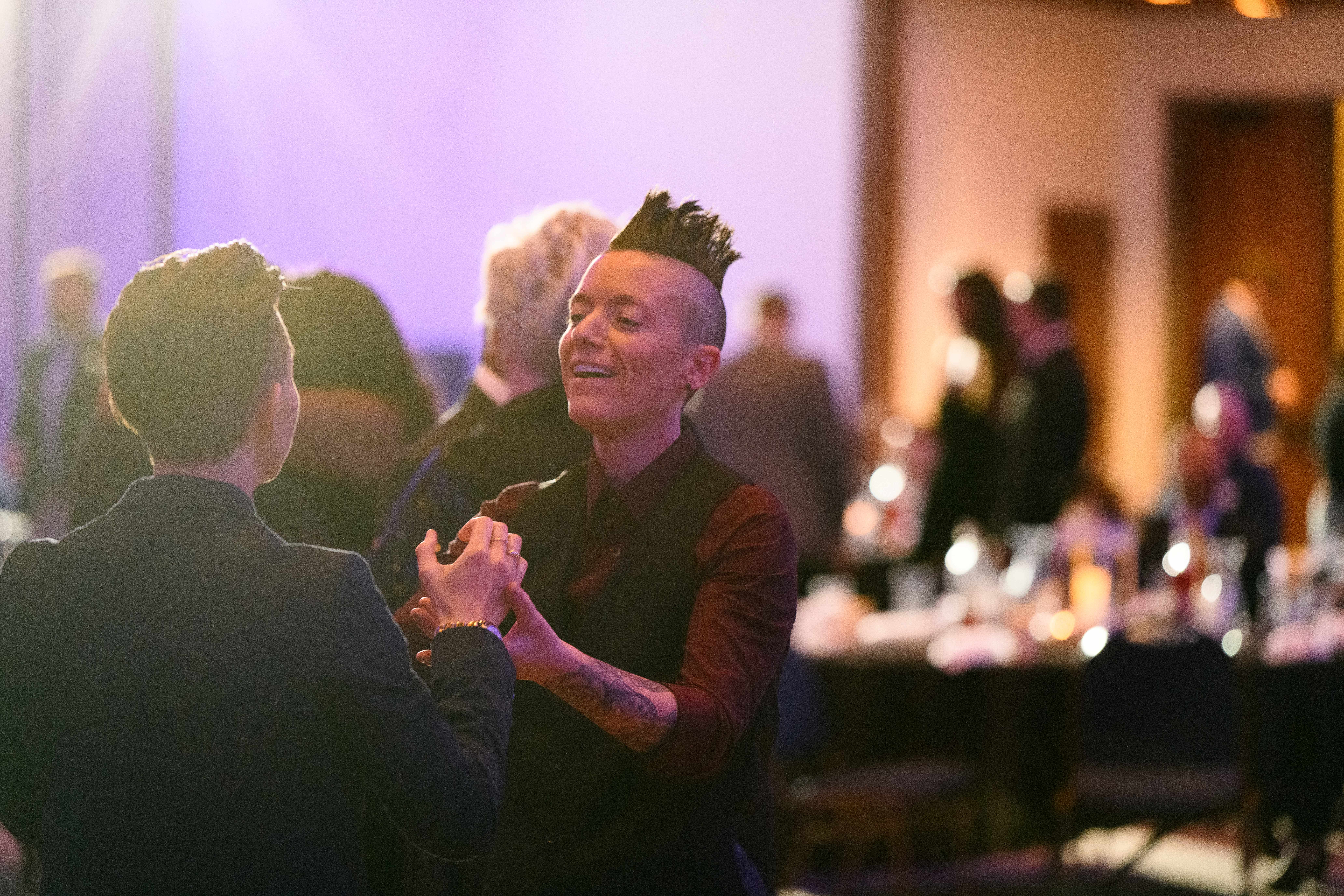 A person with a mohawk dances with another individual on the dance floor. The person facing us is expressing joy