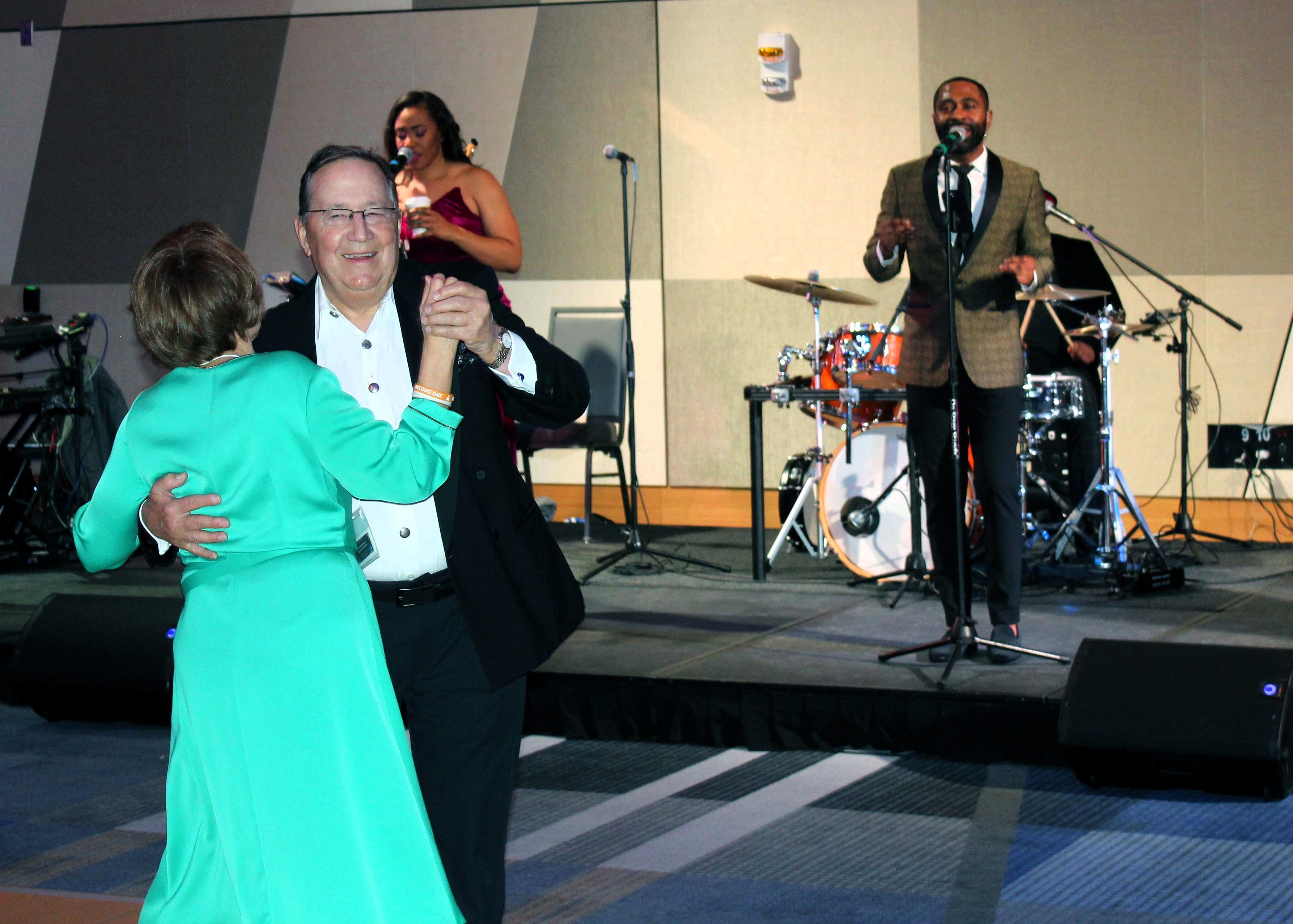 A man and woman dance together in front of a band. The man is facing the camera, and smiling