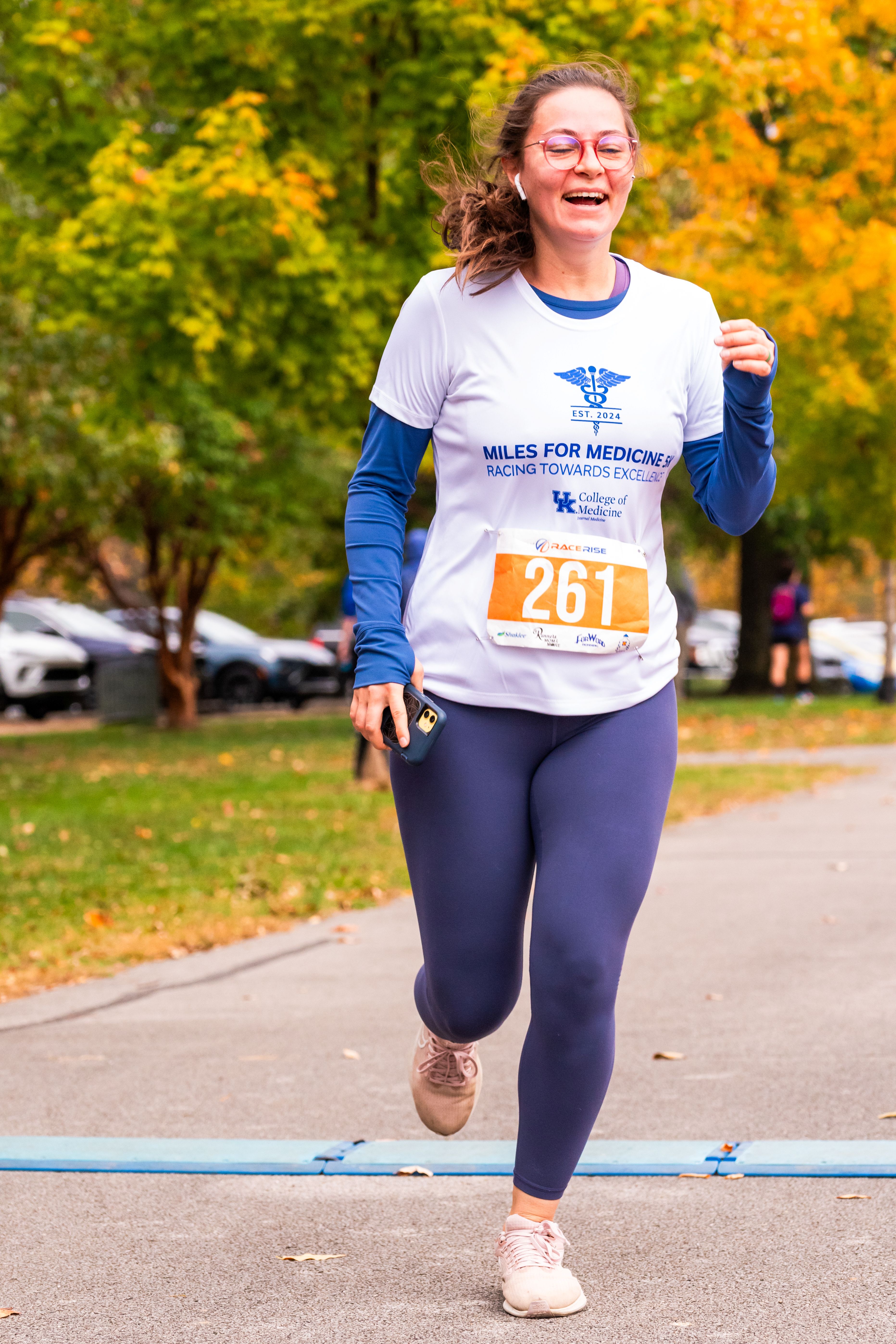 A woman with glasses runs across the finish line. She is smiling with her eyes closed.