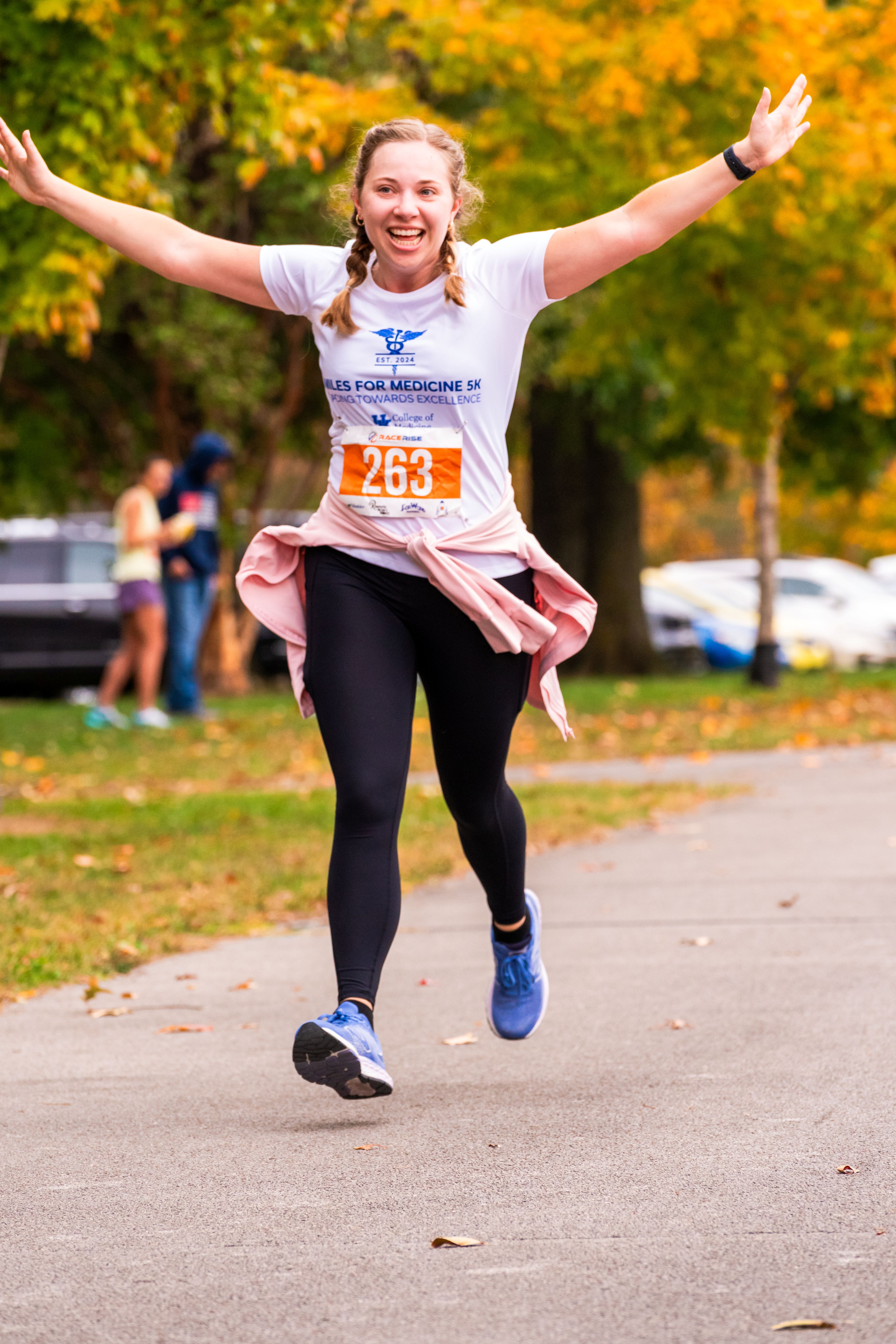 A woman runs victoriously across the concrete. Her arms are spread wide above her head as she smiles with her tongue out.