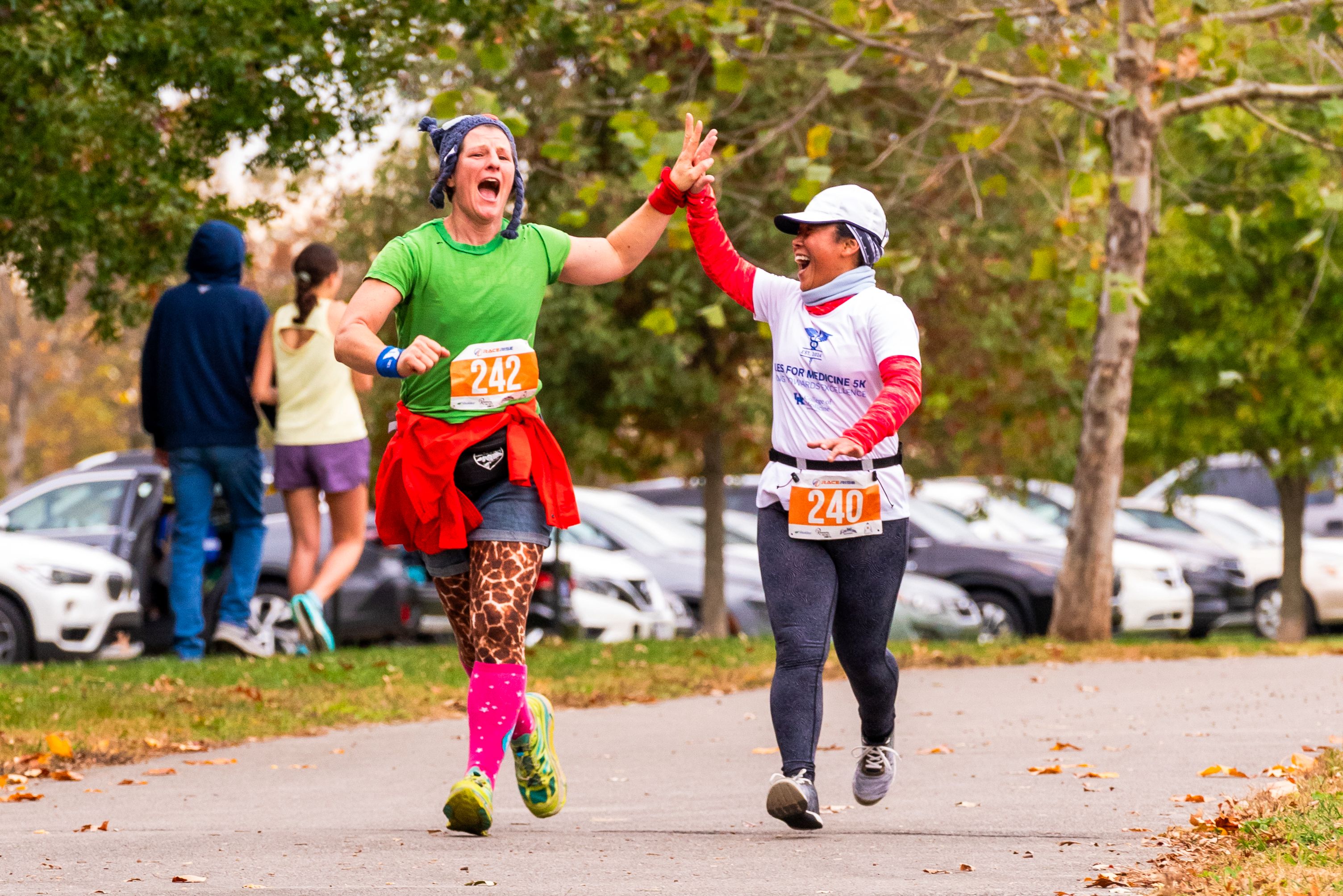 Two people high-five each other while running. One is wearing cheetah print leggings. They are both smiling.
