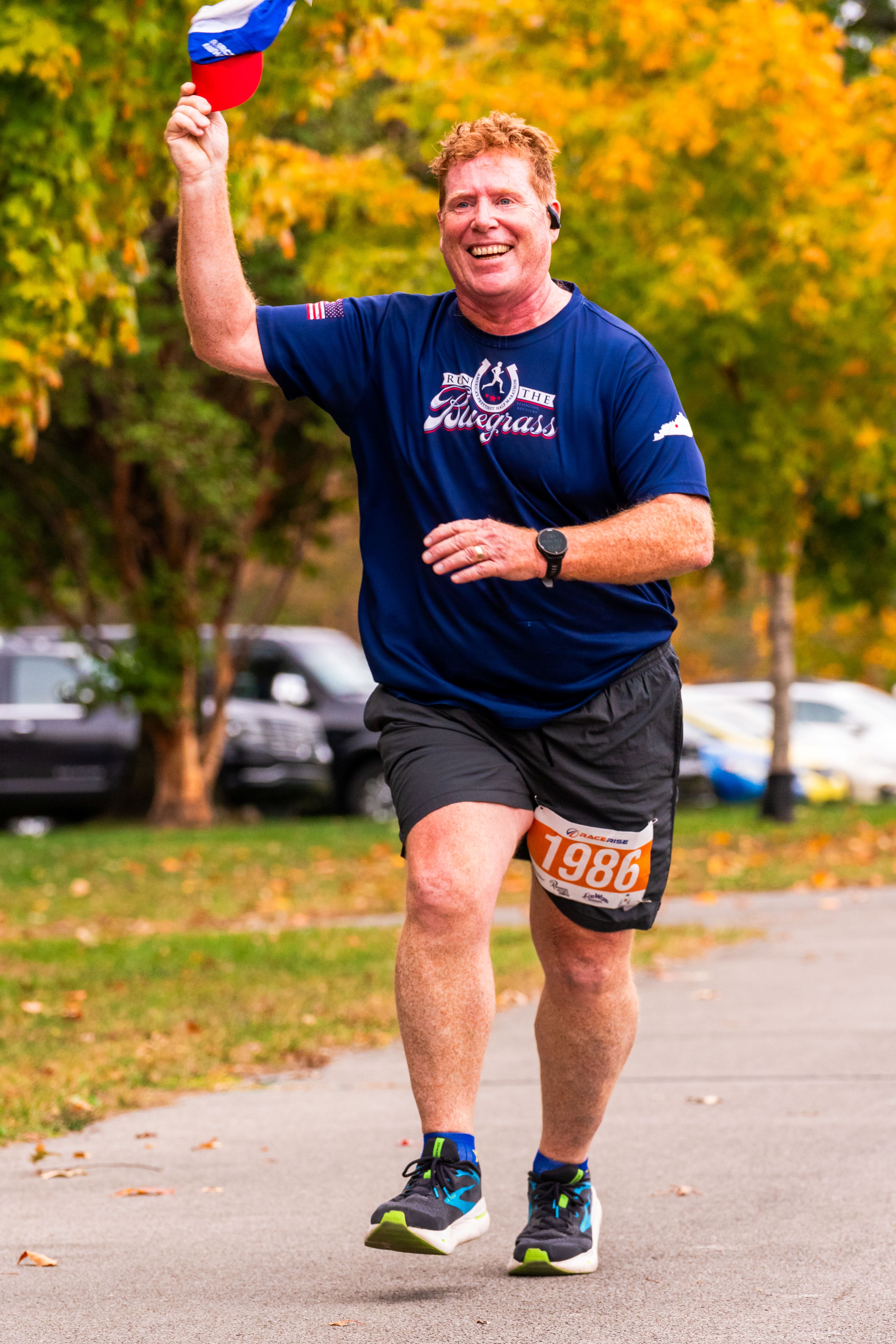 A man wearing a blue shirt runs with a smile on his face, waving his ball cap in his hand