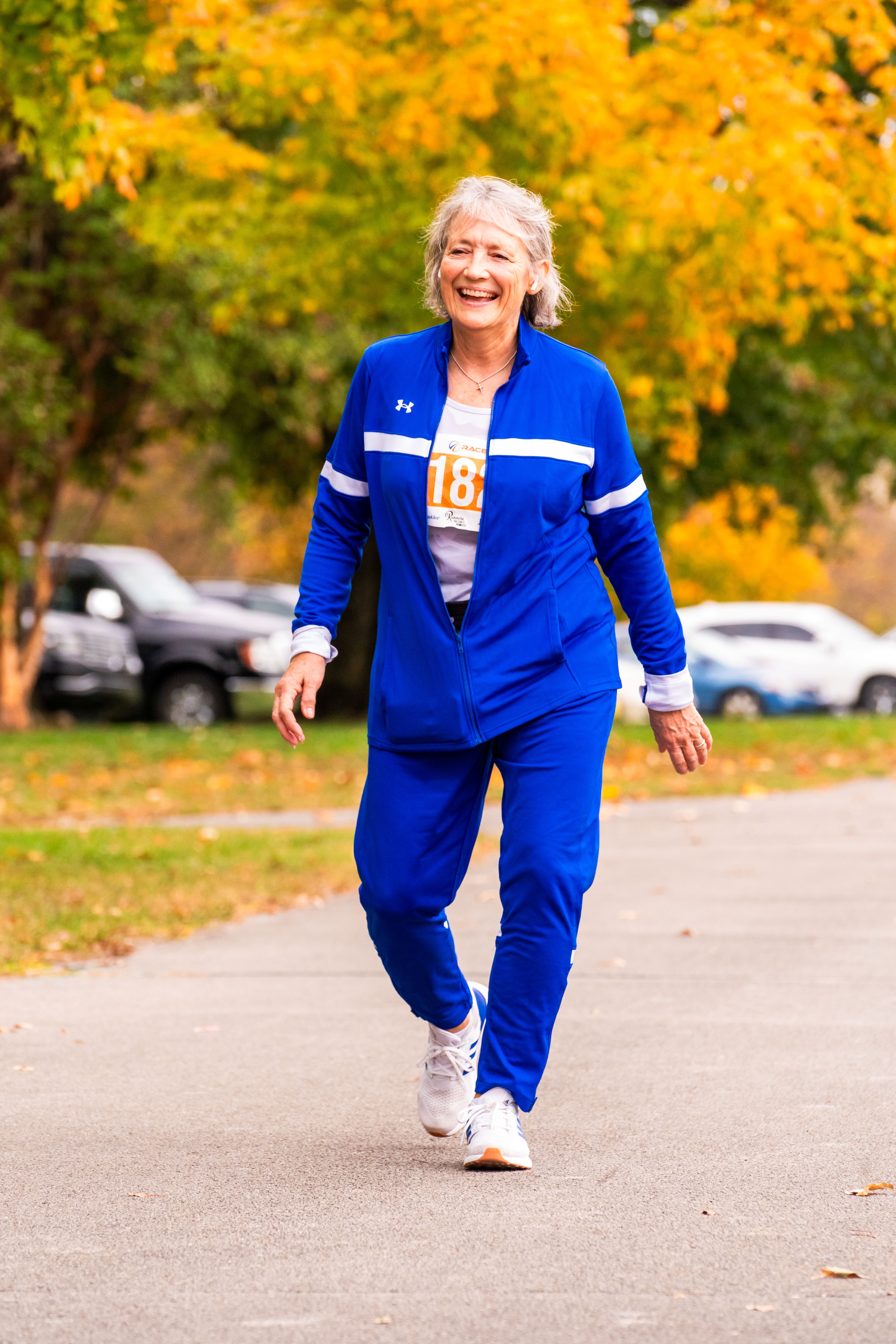 A woman in a blue tracksuit walks on the concrete. Her smile is large
