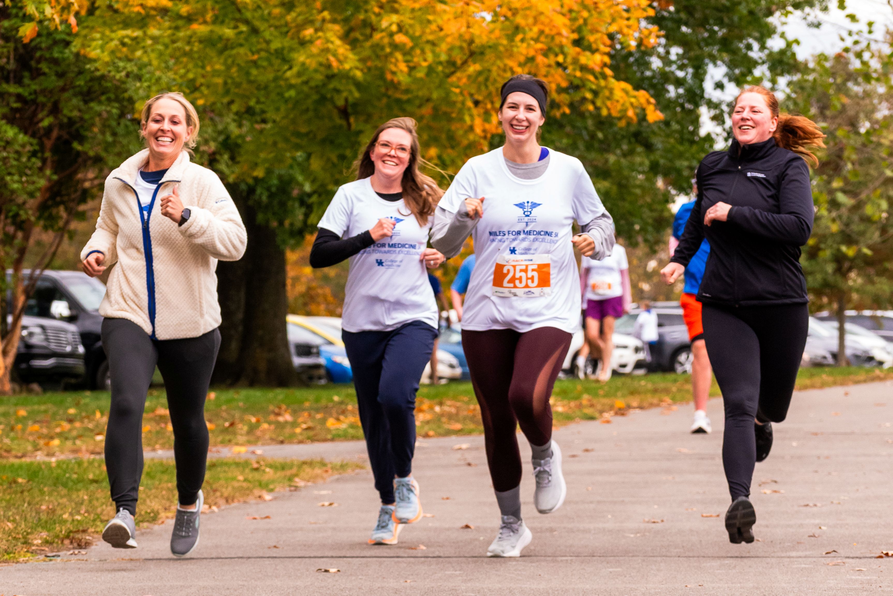 A group of four women run spryly in a line. They all have smiles on their faces. Their hair flies behind them.