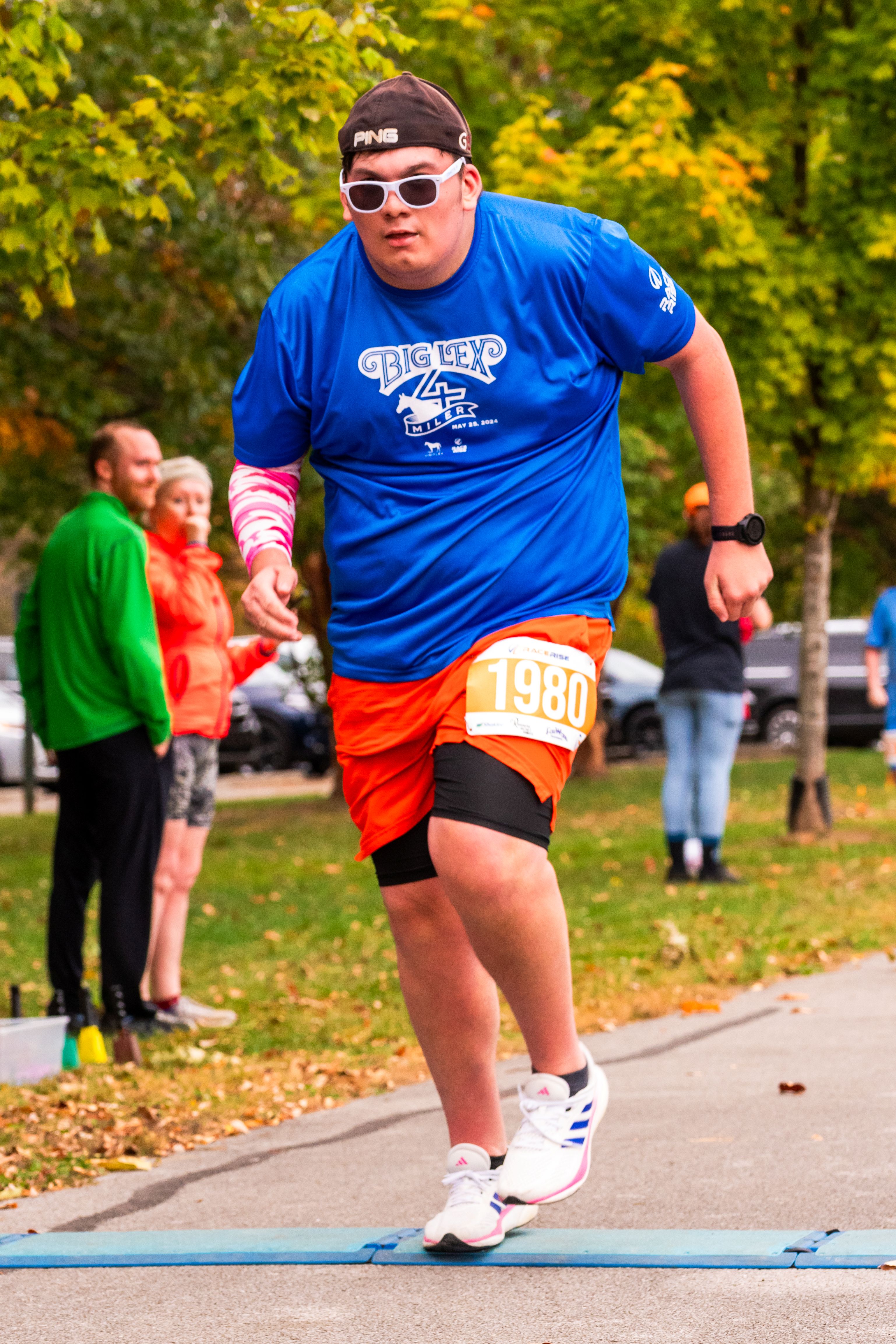 A man in sunglasses and a backwards hat runs across the finish line. His arms swing behind him.