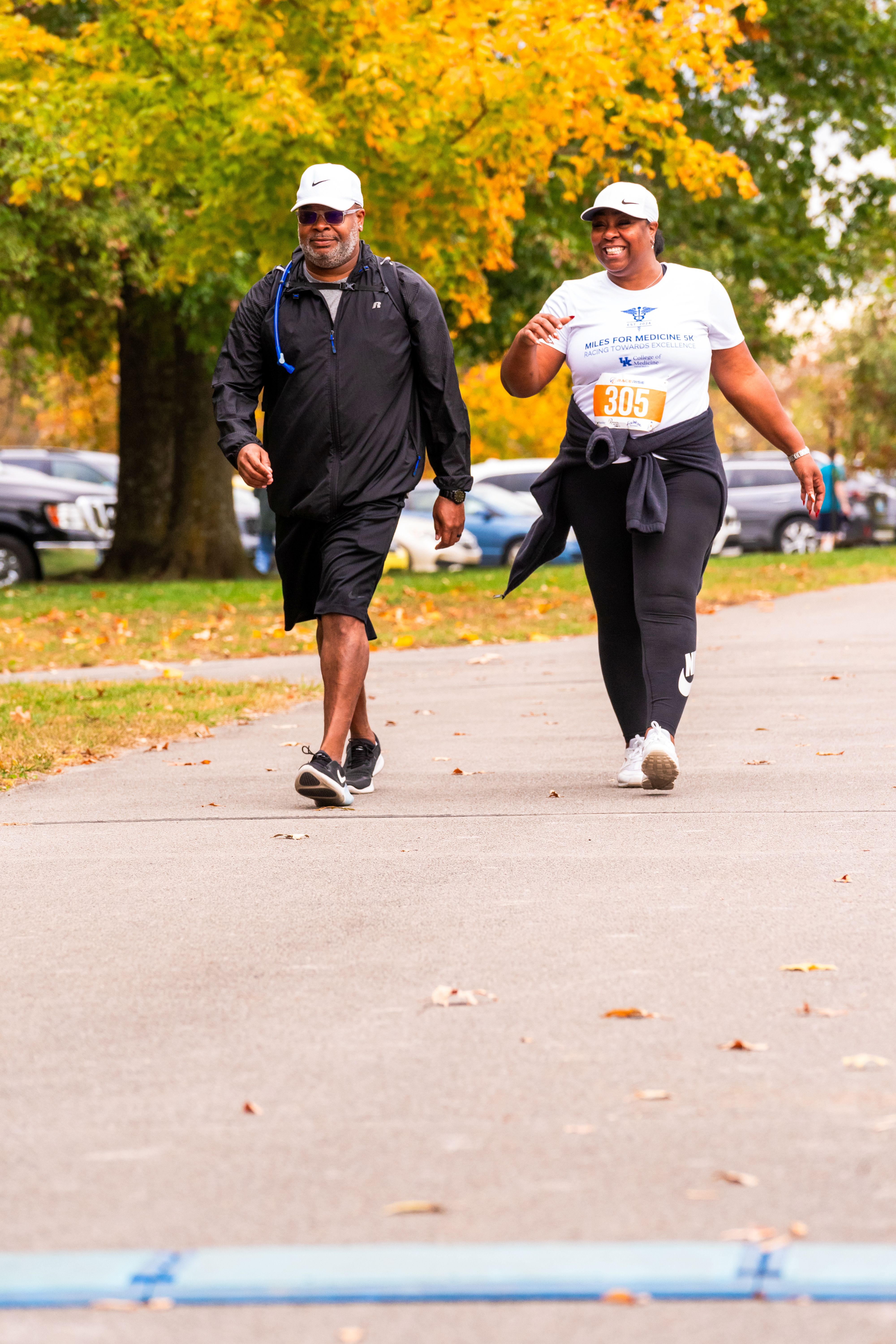 A man and a woman wearing white hats walk next to each other. The woman is smiling big