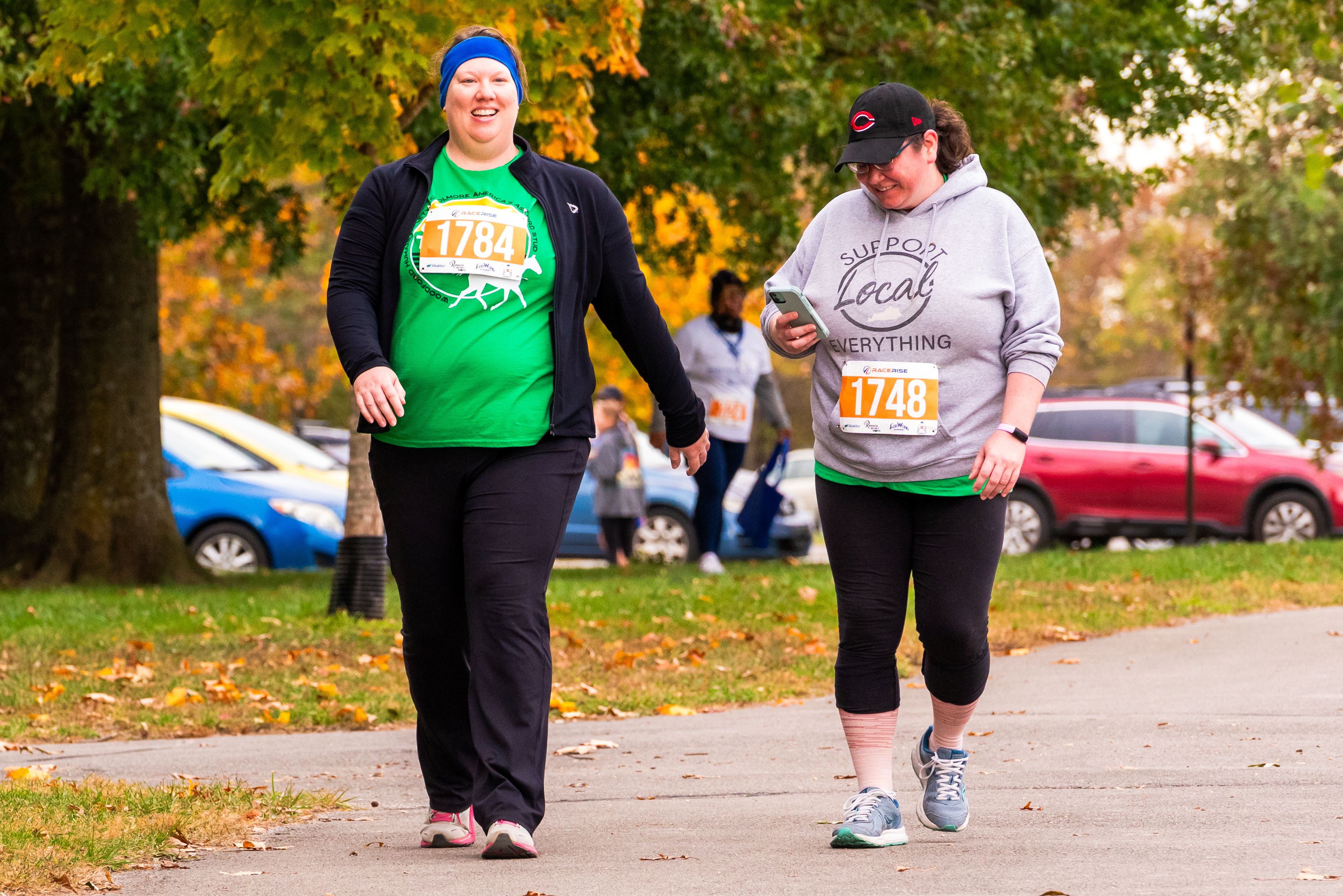 Two women smile as they walk. One of them is looking down at her phone.