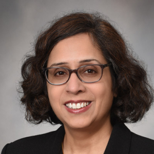 Dr. Ritu Chakravarti smiles for a headshot. She wears a black shirt and glasses.