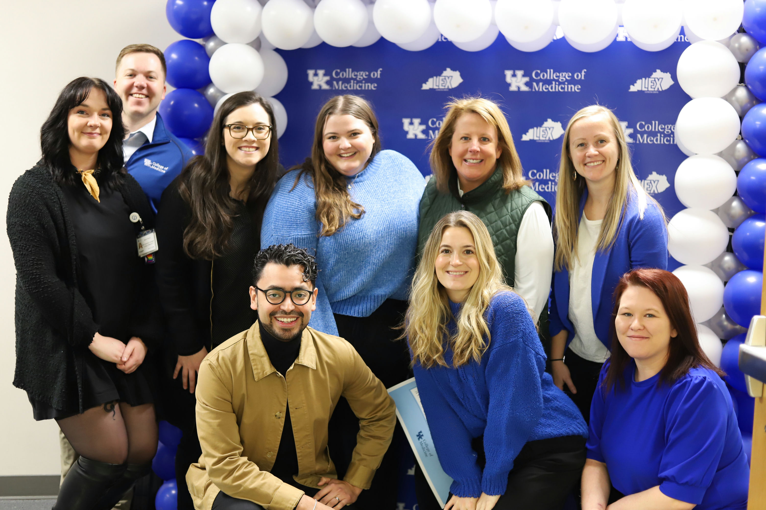 Office of Strategic Communication team poses for group photo in front of blue banner up