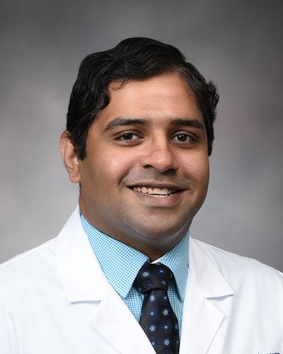 Dr. Paramarajan Piranavan smiles for a headshot. He wears a white coat, blue shirt, and black, patterned tie.
