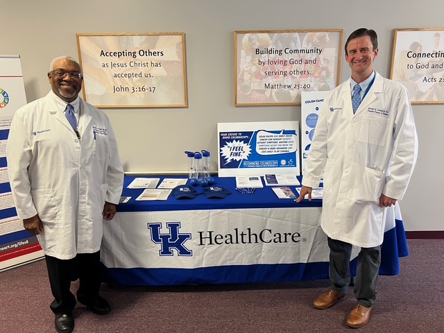 Two doctors in white coats stand flanking a table covered in informational material